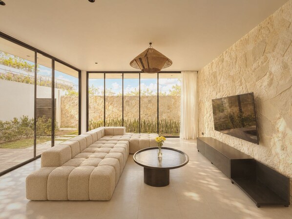 A modern living room with a sectional sofa, a round coffee table, and a flat-screen TV mounted on a textured wall.