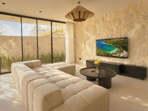 Ein modernes Wohnzimmer mit einem großen Ecksofa, einem runden Couchtisch und einem Flachbildfernseher, der an einer strukturierten Steinwand befestigt ist.