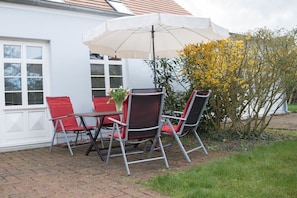 An outdoor patio with a table and four chairs, an umbrella, and a flowering plant. - "Marie" Captain's House by Petersson (Born a. Darß)