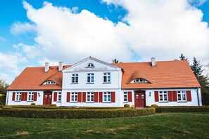 A large, white building with red shutters and a red-tiled roof. - "Marie" Captain's House by Petersson (Born a. Darß)