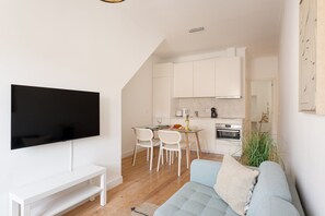 Ein modernes Wohnzimmer mit einem Flachbildfernseher, einem hellblauen Sofa und einem Essbereich mit Tisch und Stühlen.