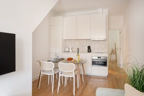 Eine kleine Küche mit weißen Schränken, einem Esstisch mit Stühlen, einer Kaffeemaschine und einem Backofen.