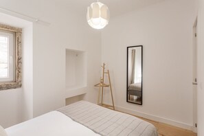 Ein Schlafzimmer mit einem Bett, einer Hängelampe, einem Spiegel und einem Holzstuhl.