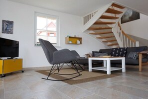 A modern living room with a television, a rocking chair, a sofa, a coffee table, and a staircase. - Thatched house "De Leevde" (Zierow)