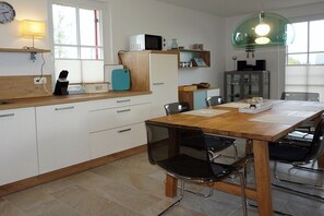 A modern kitchen with white cabinets, a wooden countertop, a dining table with chairs, and a green pendant light. - Thatched house "De Leevde" (Zierow)