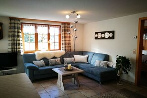 A living room with a blue sofa, a small table, a television, and a plant. - Holiday apartment with 1 bedroom (Grindelwald)