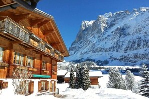 A wooden chalet with a balcony, surrounded by snow-covered trees and mountains. - Holiday apartment with 1 bedroom (Grindelwald)