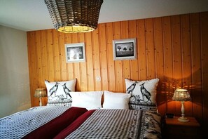 A room with wooden panel walls, a bed with patterned bedding, two wall-mounted lamps, and two framed pictures. - Holiday apartment with 1 bedroom (Grindelwald)