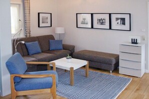 A living room with a sofa, armchair, coffee table, and a small cabinet. - Holiday home with 3 bedrooms (Timmendorfer Strand)