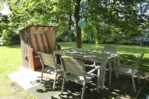 An outdoor dining area with a table and chairs, surrounded by greenery and a tree. - Buoy in the house Sanddorn (Ahrenshoop)