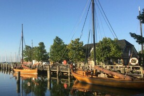 Un port esportiu amb vaixells de fusta amarrats, un moll de fusta i una casa amb un rellotge.
