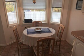 A dining area with a round table, four chairs, and a window with blinds. - terraced house Grüner Weg (Fehmarn)