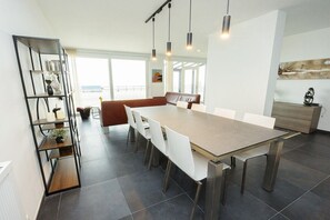 A modern dining area with a long table, white chairs, and pendant lighting. - Holiday home in Middelkerke with Wi-Fi (Middelkerke)