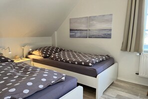 A bedroom with two beds, a nightstand, a lamp, and a view of the outside. - Holiday apartment with 1 bedroom (Fehmarn OT Klausdorf)