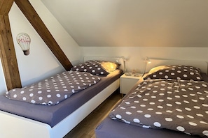 A small, cozy room with two single beds, each with a polka dot duvet and pillow. There is a nightstand with a lamp and a small decorative item between the beds. - Holiday apartment with 1 bedroom (Fehmarn OT Klausdorf)