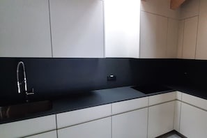 A modern kitchen with white cabinetry, a black countertop, and a stainless steel sink. - Casa Labhardt, 1st floor (Lugano Castagnola)
