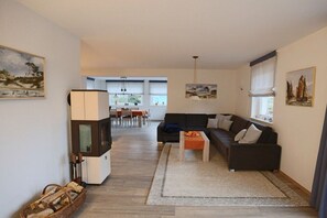 A living room with a sofa, coffee table, and a television. There is a dining area in the background with a table and chairs. - Holiday home with 1 bedroom (Born a. Darß)
