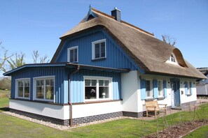 A traditional house with a thatched roof, a blue exterior, and a brick foundation. - Holiday home with 1 bedroom (Born a. Darß)