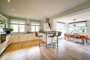 A modern kitchen with a central island, bar stools, and a dining area with a table and chairs. - Holiday home with 1 bedroom (Born a. Darß)