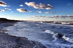 A beach with waves, a clear sky, and a distant shoreline. - Holiday home with 1 bedroom (Born a. Darß)