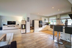 A modern kitchen with a central island, bar stools, and a dining area with a bench. - Holiday home with 1 bedroom (Born a. Darß)