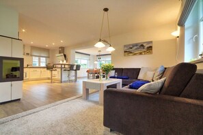 A modern living room with a sofa, a coffee table, and a kitchen in the background. - Holiday home with 1 bedroom (Born a. Darß)