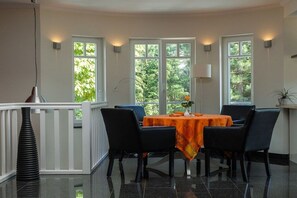 A dining area with a table set for four, surrounded by chairs, with windows offering a view of greenery outside. - Holiday apartment with 2 bedrooms (Dierhagen)