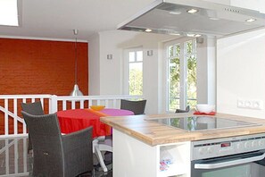 A kitchen with a central island, a dining area with chairs and a table, and a view of greenery outside. - Holiday apartment with 2 bedrooms (Dierhagen)