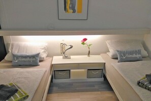 A hotel room with two beds, each with a pillow labeled 'Heimathafen,' a bedside table with a vase and a flower, and a wall-mounted artwork. - Dream view "Nautilus" (Sierksdorf)