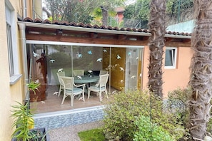 Een terras met een glazen deur, een tafel met stoelen en een kleine tuin met planten en een palmboom.