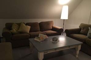 Ein Wohnzimmer mit braunen Sofas, einem Couchtisch mit einem Buch und einem Glas sowie einer Stehlampe.