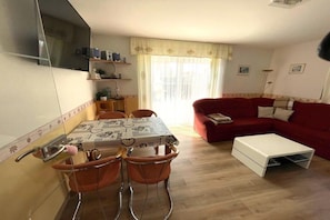 A living room with a red sofa, a white coffee table, and a dining area with a table and chairs. - 10 holiday apartment "Anders Fewo 1" (Burg auf Fehmarn)