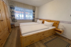 A bedroom with a wooden bed, a nightstand, a lamp, a wardrobe, and a window with curtains. - 10 holiday apartment "Anders Fewo 1" (Burg auf Fehmarn)