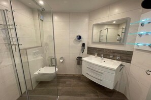 Un baño moderno con cabina de ducha de vidrio, un lavabo blanco con espejo y un mueble con cajones.