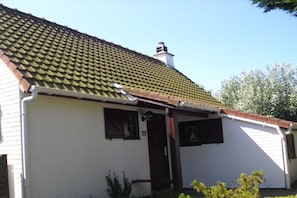 A white building with a tiled roof, a chimney, and a small porch with a door and windows. - Holiday home in Bredene with swimming pool (Bredene)