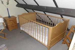 A wooden crib in a room with a sloped ceiling, a small wooden dresser, and a vase with a plant. - Holiday home in Bredene with swimming pool (Bredene)
