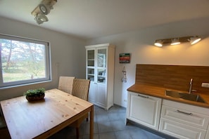 A kitchen with a wooden table, white cabinets, a window, and a sign on the wall. - Bodden view with sauna (Pruchten)