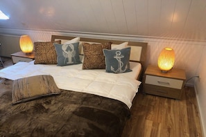 A bed with a white comforter and multiple pillows, including a decorative anchor design. There are two bedside tables with lamps, and a wooden headboard. - Bodden view with sauna (Pruchten)
