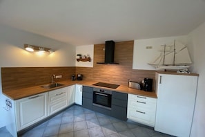 Eine kleine Küche mit einer Holzarbeitsplatte, einem eingebauten Backofen und einem Schiffmodell an der Wand.