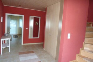 A hallway with a red wall, a wooden staircase, and a door leading to another room. - Bodden view with sauna (Pruchten)