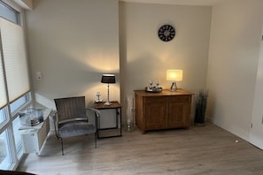 Ein Zimmer mit einem Holzschrank, zwei Stühlen, einem kleinen Tisch mit Lampe und einer Wanduhr.