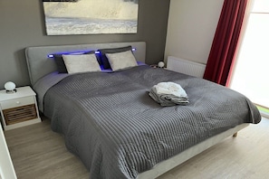Ein ordentlich bezogenes Bett mit einer grauen Tagesdecke, einem Kissen und einem gefalteten Handtuch.