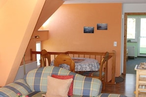 Ein gemütliches Zimmer mit schrägem Dach, einem hölzernen Bett, einem karierten Sofa und zwei gerahmten Bildern an der Wand.