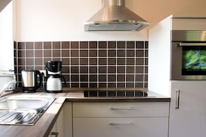 A modern kitchen with a stainless steel range hood, a built-in oven, and a coffee maker on the countertop. - The small holiday apartment (Prerow)