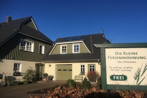 A two-story house with a green exterior and a sign advertising a small residential property for two people. - The small holiday apartment (Prerow)