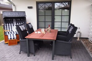 Eine Terrasse im Freien mit einem Holztisch und vier schwarzen Korbstühlen.