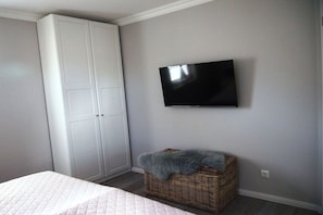 A bedroom with a bed, a wardrobe, a television, and a wicker basket with a blanket. - Holiday apartment with 2 bedrooms (Zingst)