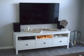 A white entertainment unit with a flat-screen TV mounted above it, a speaker, and a decorative item on the shelf. - Holiday apartment with 2 bedrooms (Zingst)