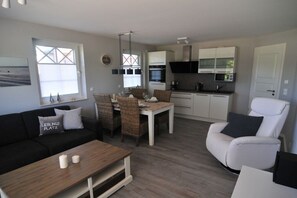Ein modernes Wohnzimmer mit einer Couch, einem Esstisch und Stühlen, einer Küche mit Geräten und einem weißen Sessel.