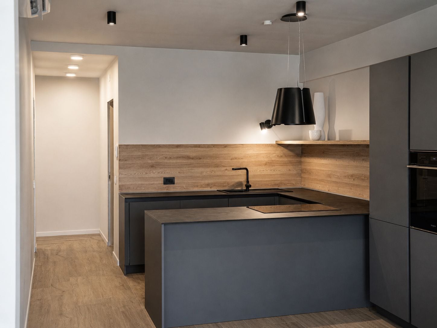A modern kitchen with a central island, a built-in oven, and a pendant light.
